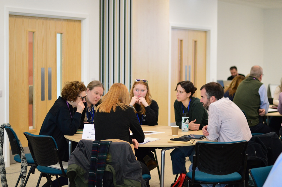 6 people sitting around round table deep in discussion together 